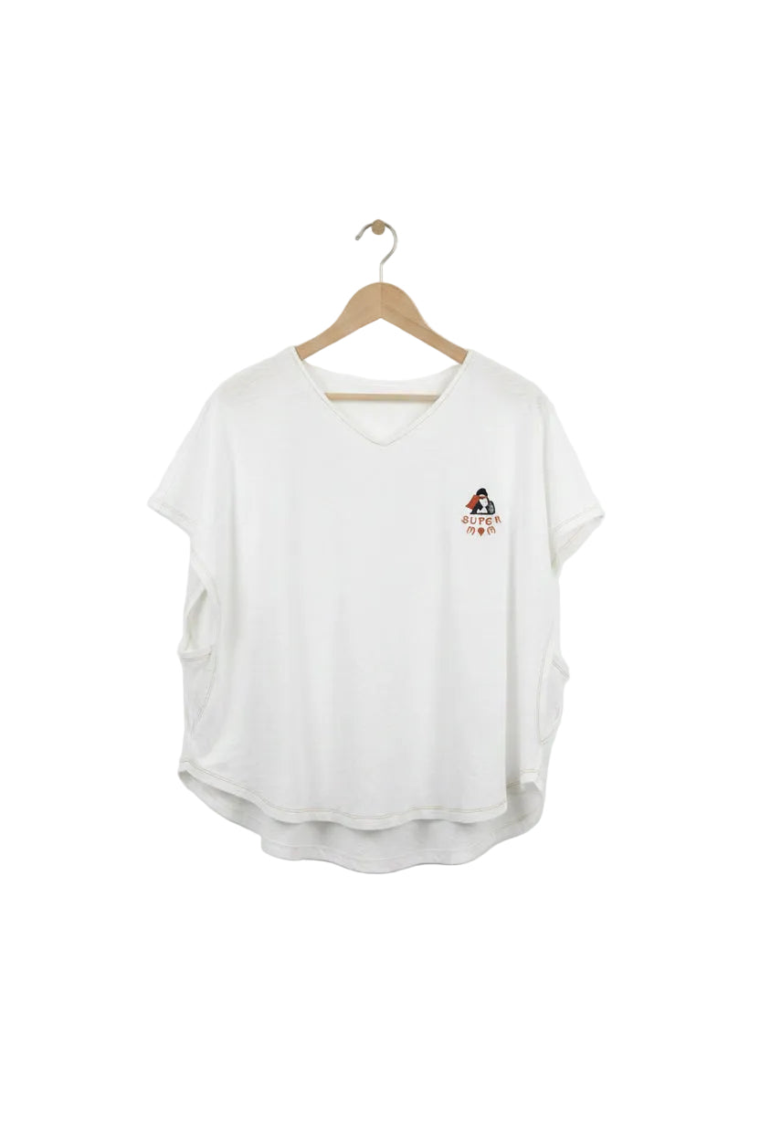 White t-shirt with a small graphic on a hanger against a plain wall.